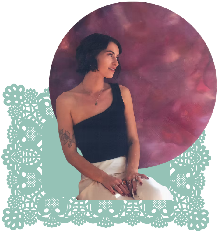 Caroline seated in front of a pink painted backdrop, framed by teal lace